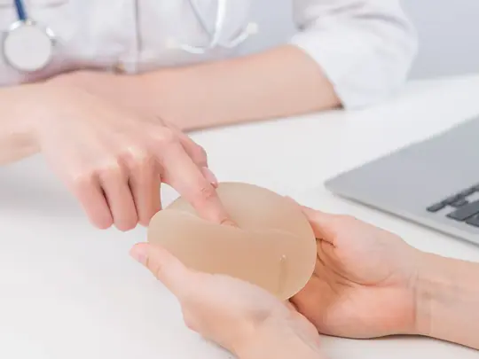 Clinician placing a breast implant in a patient's hand across a consultation desk